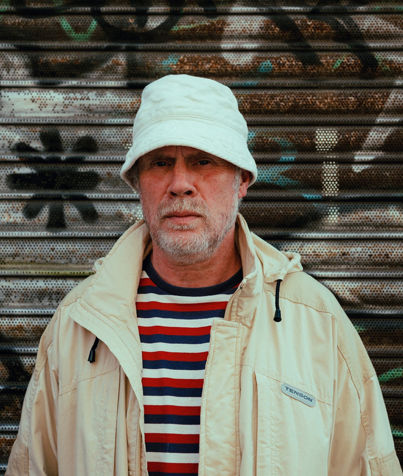 Oi Polloi co-founder in a pale bucket hat, striped T-shirt and lightweight jacket on Manchester’s Tib Street.