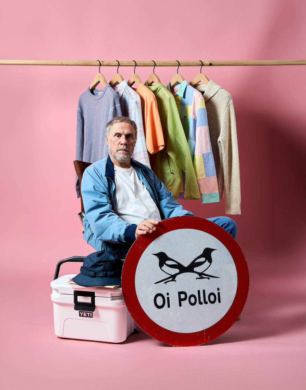 Oi Polloi co-founder Nigel Lawson sitting on a pink YETI cooler beneath a rail of colourful clothing and an Oi Polloi sign