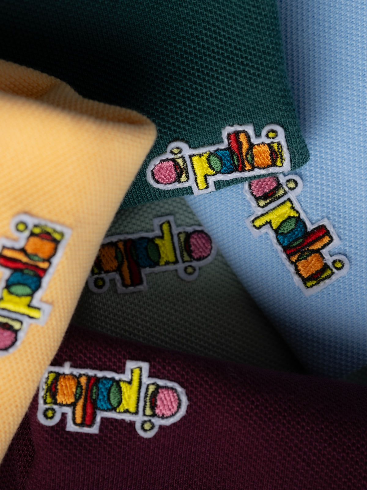 Oi Polloi embroidered logo labels on green, blue, yellow and burgundy fabric in a close-up product detail shot