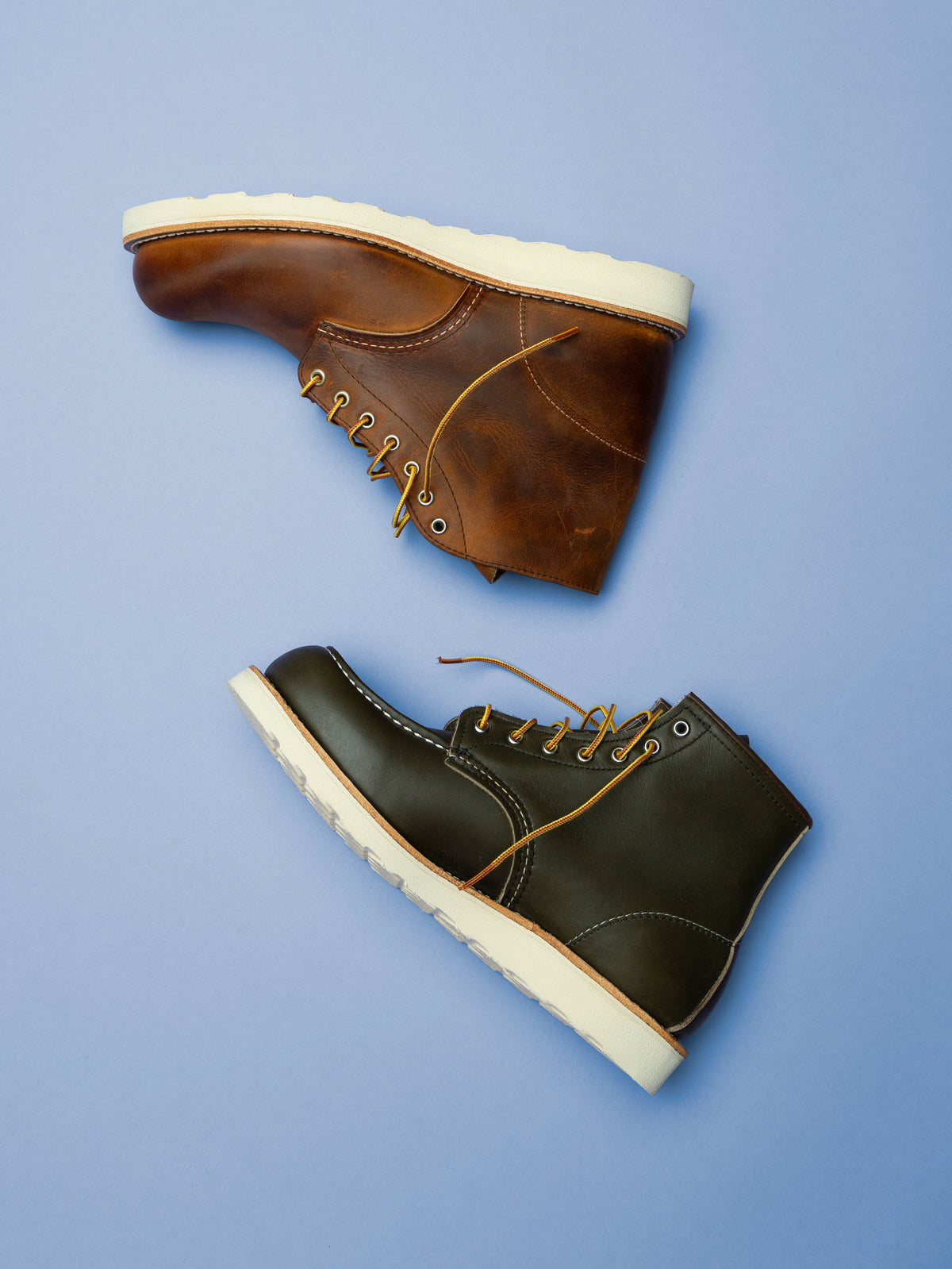Red Wing leather boots in brown and black with contrasting white soles, photographed against a blue background